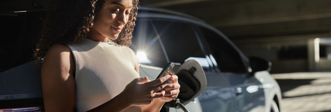 Female researching on her mobile device while her electric vehicle is charging