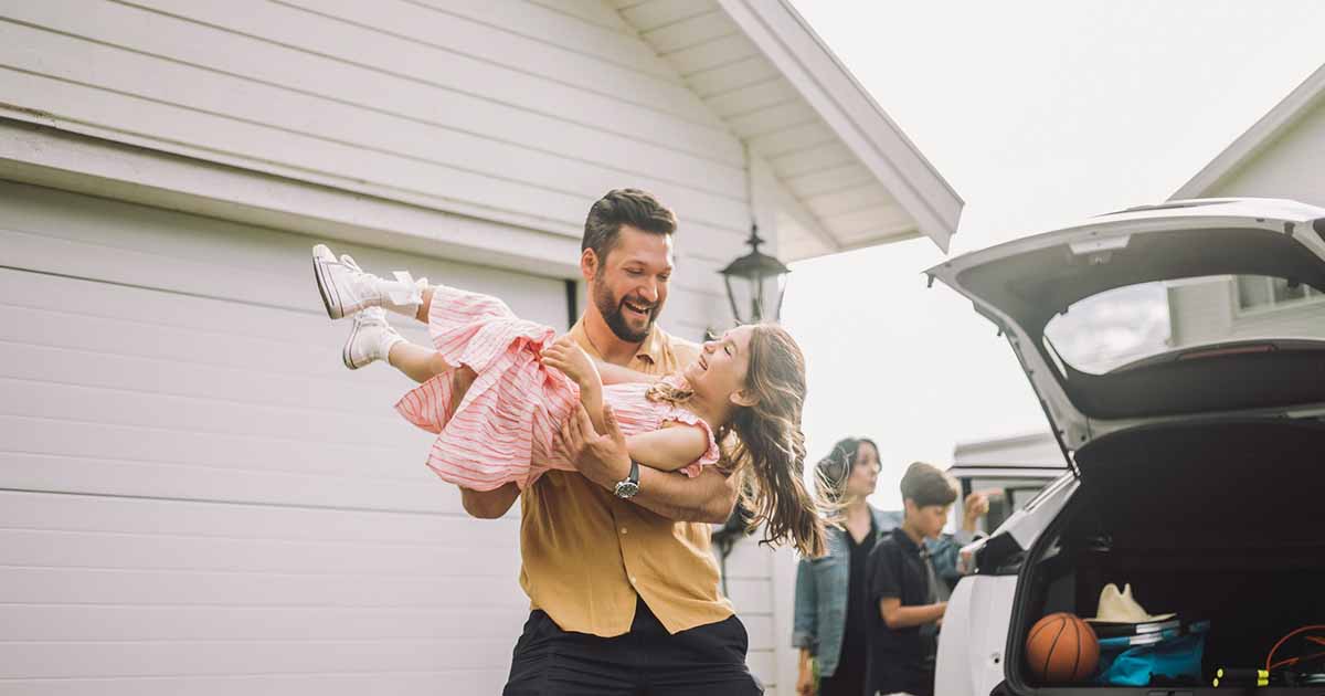 A smiling man carries his laughing daughter